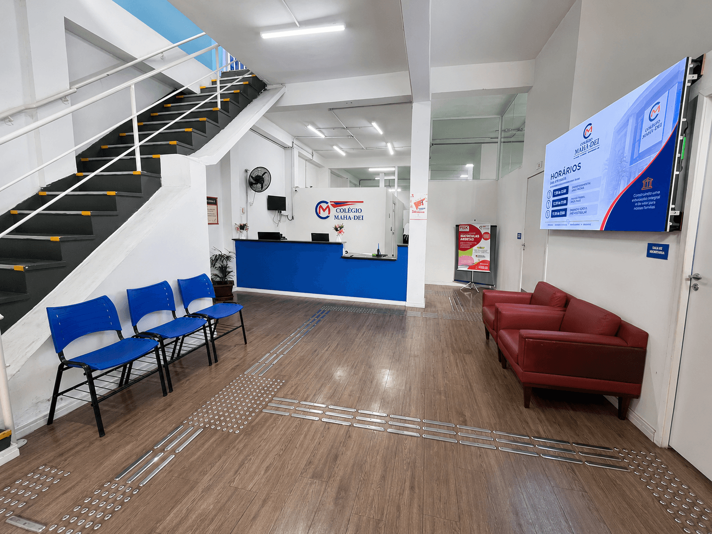 Recepção acolhedora do Colégio Maha Dei com piso tátil e painel digital na Vila Galvão